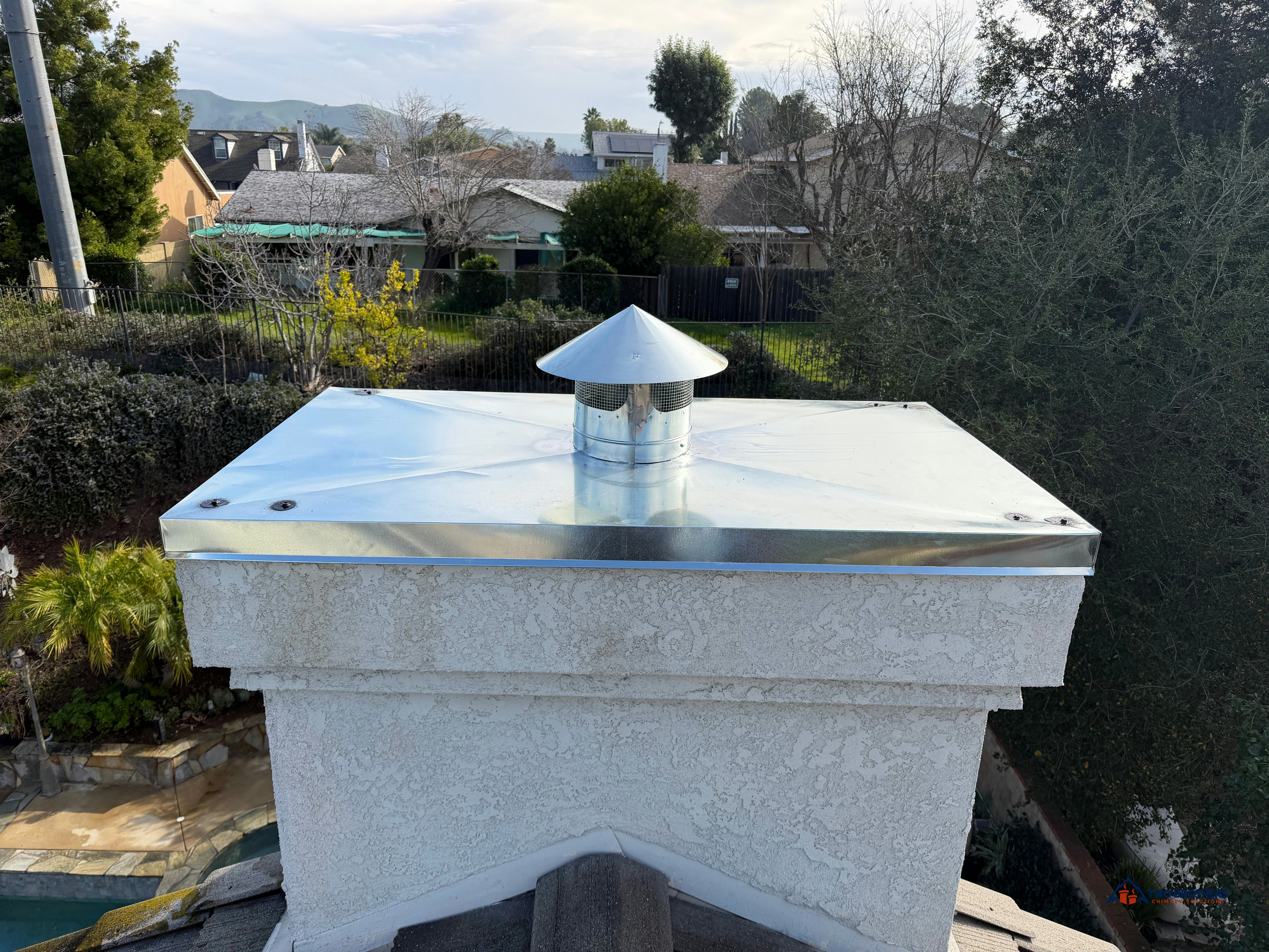 Metal chase cover and round chimney cap above a stucco chimney
